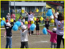 青と黄色のポンポンを持って踊る園児たち